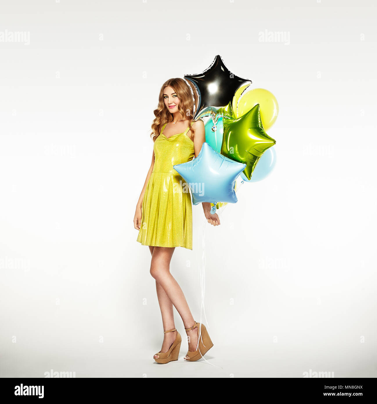 Schöne junge Frau mit bunten Luftballons auf einem weißen Hintergrund. Geburtstag und Party. Mädchen im grünen Kleid auf dem Festival Stockfoto