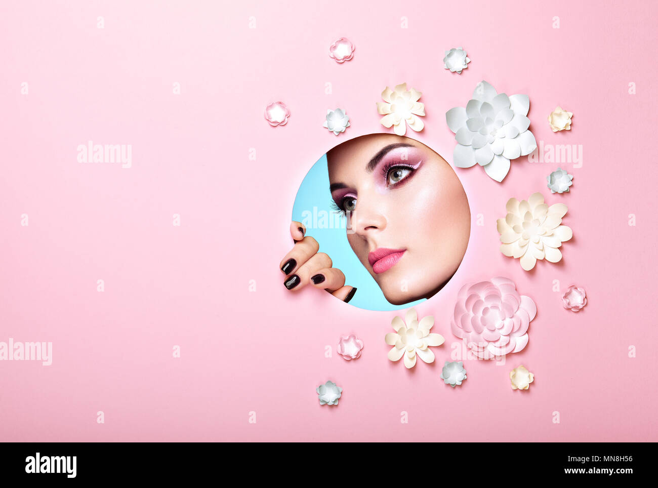 Konzeptionelle Schönheit Porträt der schönen jungen Frau. Angesichts der Mädchen mit Frühling rosa Make-up. Beauty Fashion Model Frau Gesicht perfekte Haut. Papier Blumen auf rosa Hintergrund Stockfoto