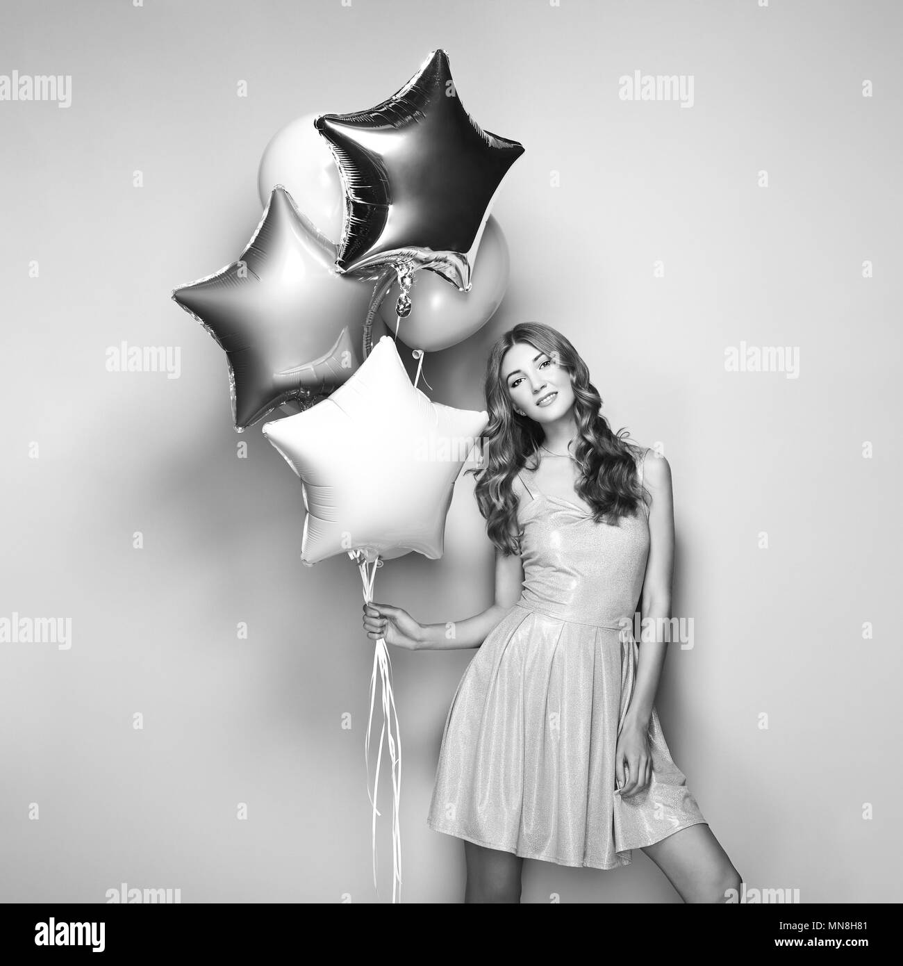 Schöne junge Frau mit Ballons auf einem weißen Hintergrund. Geburtstag und Party. Mädchen in graues Kleid auf dem Festival. Schwarz und Weiß Foto Stockfoto
