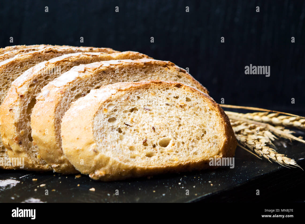 Weizen Scheiben Brot auf einem dunklen Schneidebrett Stockfoto