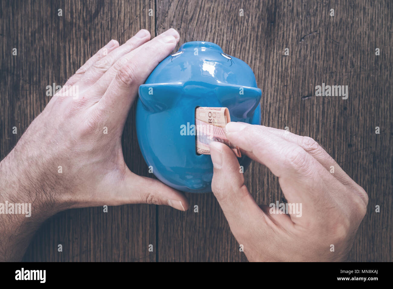Hand der männlichen Person Geld in Sparschwein Einsparungen Konzept Stockfoto