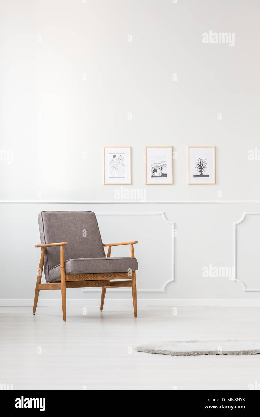 Grau Sessel gegen weiße Leiste an der Wand mit Plakaten in einfachen Wohnzimmer Innenraum Stockfoto