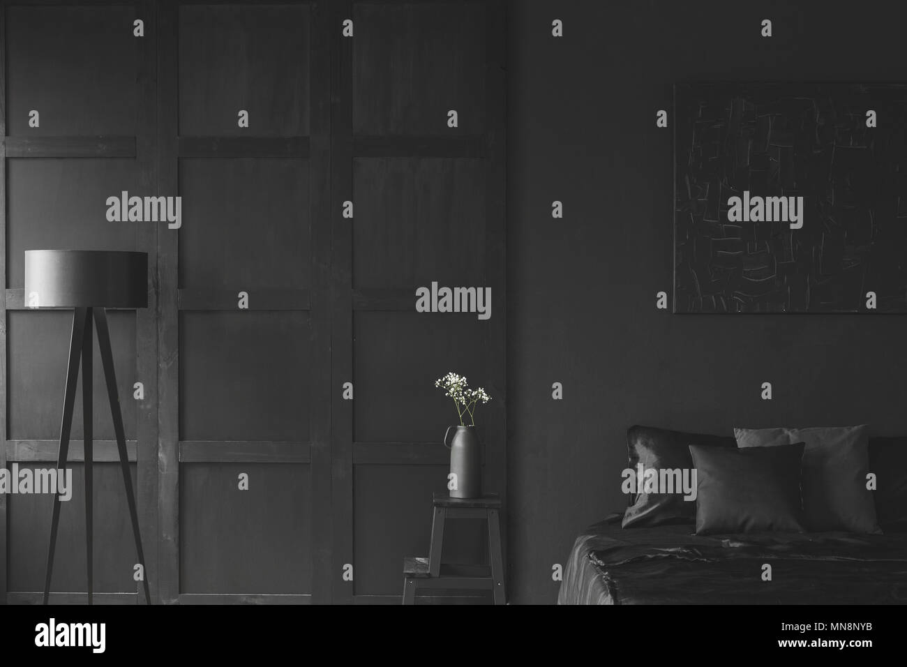 Weiße Blumen auf dem Tisch zwischen Lampe und Bett im Schlafzimmer schwarz Interieur mit Leiste an der Wand Stockfoto