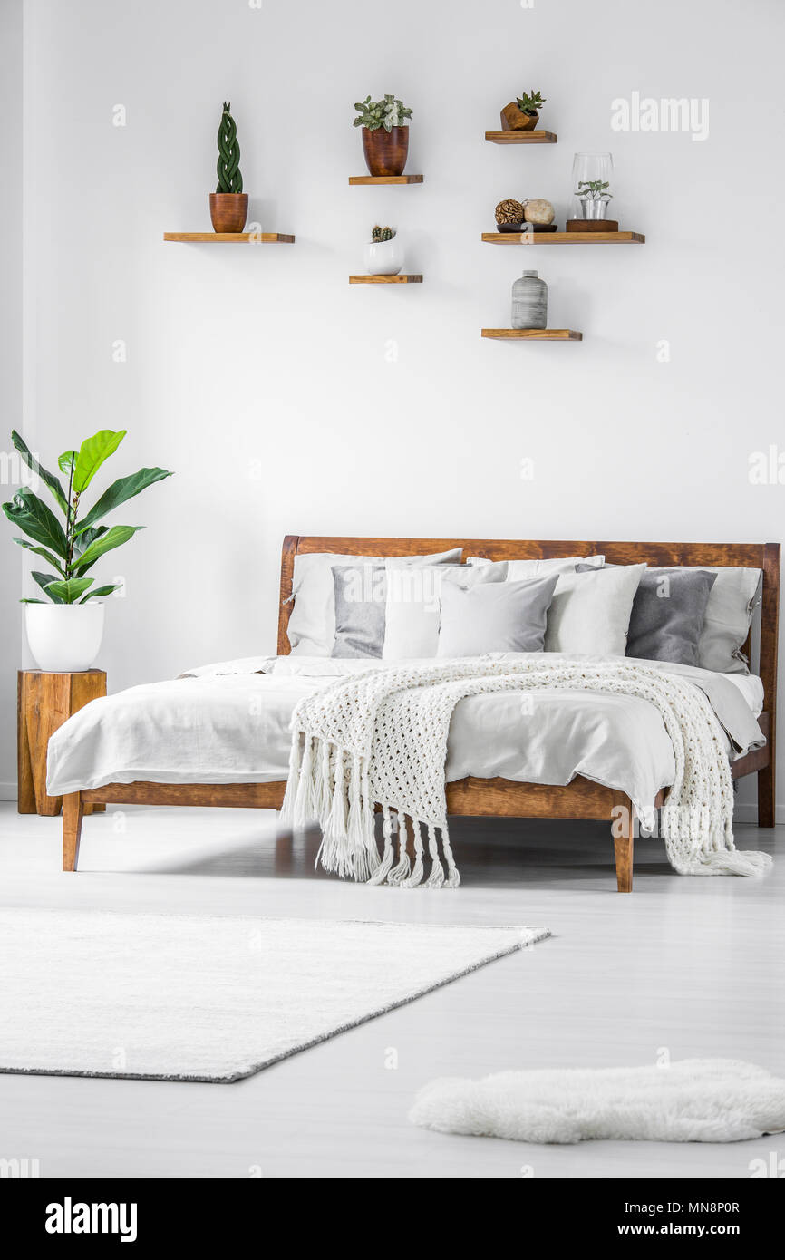 Anlage auf hölzernen Hocker neben dem Bett mit Stricken Decke in einfachen weißen Schlafzimmer Innenraum Stockfoto