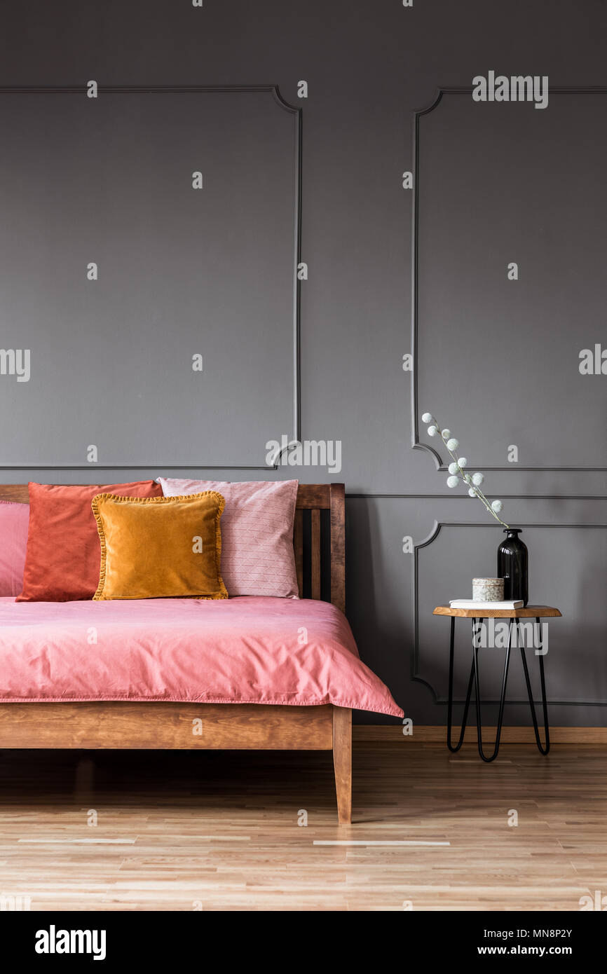 Bunte Kissen auf Rosa Bett aus Holz in Grau Schlafzimmer Innenraum mit molding Wand und Tisch Stockfoto