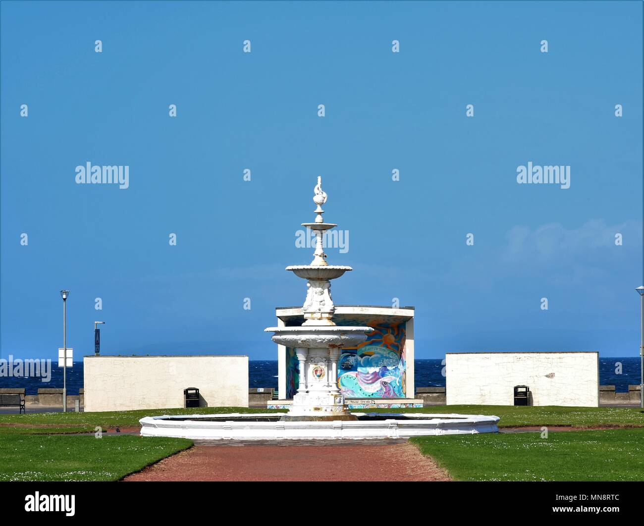 Springbrunnen und Schutz mit Kunst an der Strandpromenade mit Blick aufs Meer im Hintergrund vor blauem Himmel in Ayr, Schottland, UK gemalt. Stockfoto