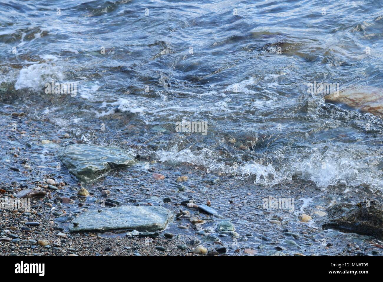 Sanfte Wellen gegen kleine Felsen auf einer peddle Strand an einem sonnigen Tag. Stockfoto