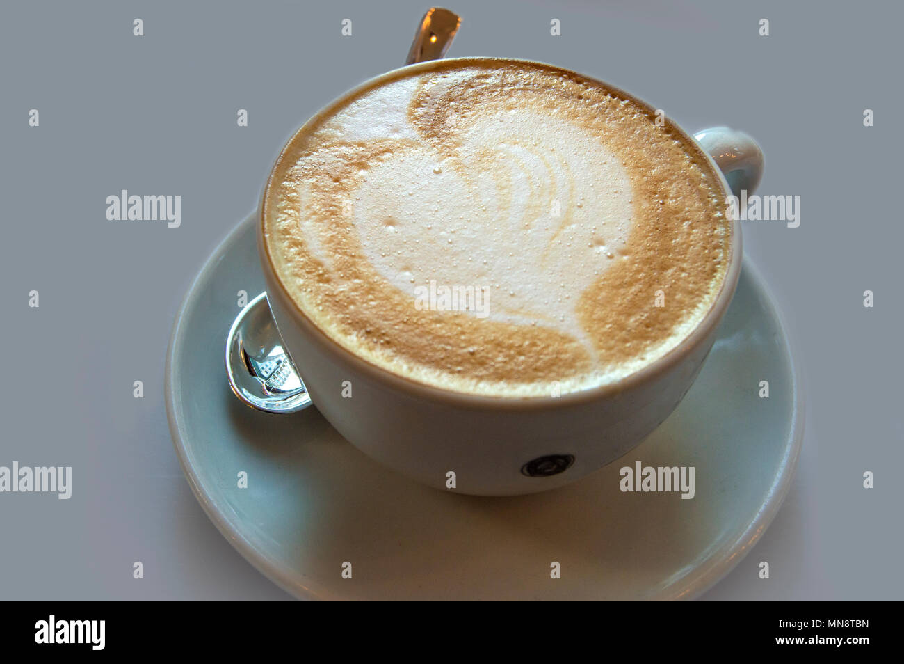 Eine Tasse Kaffee mit Milch und Teelöffel auf neutralem Hintergrund isoliert. Stockfoto