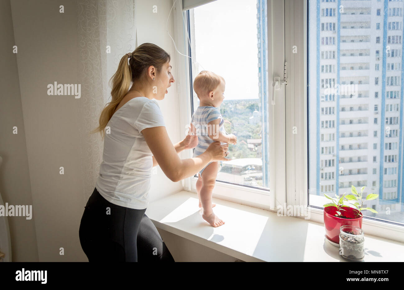 Mutter hetzen, um zu Ihrem baby boy auf der Fensterbank. Konzept der Baby in Gefahr Stockfoto