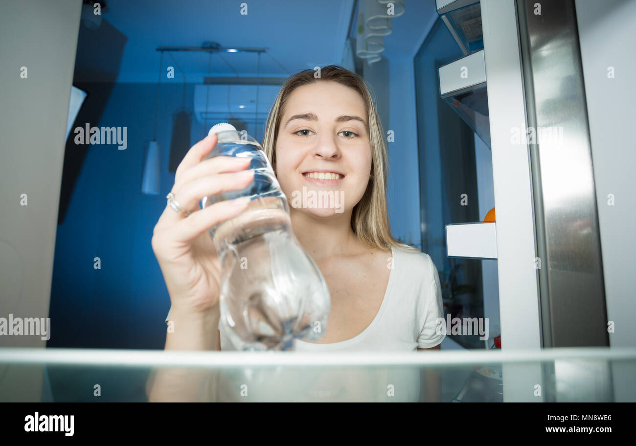 Portrait der junge blonde Frau Hunger, die Flasche Wasser aus dem Kühlschrank in der Nacht Stockfoto