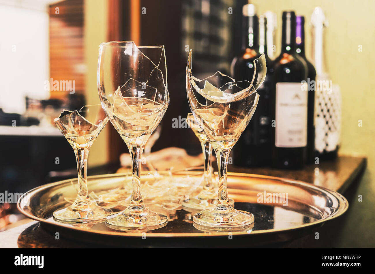 Gebrochene Glas Wein auf einem Tablett mit etwas Wein und Champagner Flaschen unscharf im Hintergrund. Gebrochene Glas eine Party oder Feier. Stockfoto