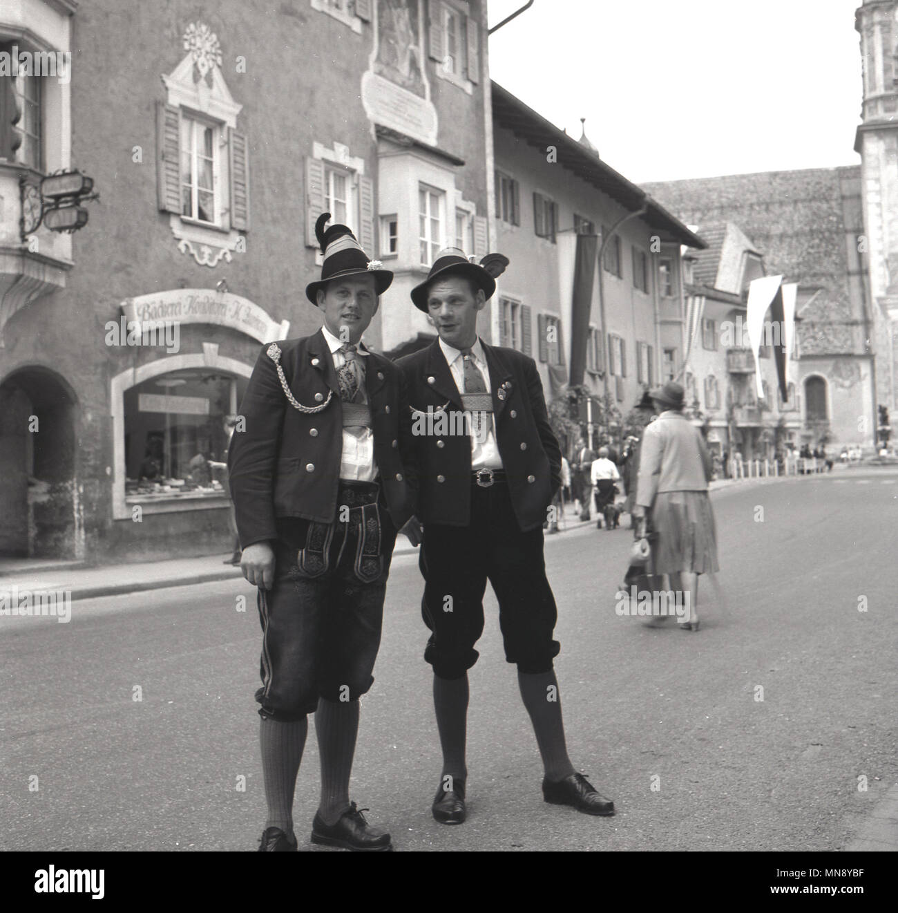 1950er Jahre, Deutschland, zwei Männer zusammen draußen auf der Straße stand das Tragen der traditionellen bayerischen Kleidung der Epoche, eine Form von Lederhosen, bekannt als Bundhosen. Hier sind sie elegant in die vollständige Outfit gekleidet, der knielange Hose mit Jacken und Mützen. Stockfoto