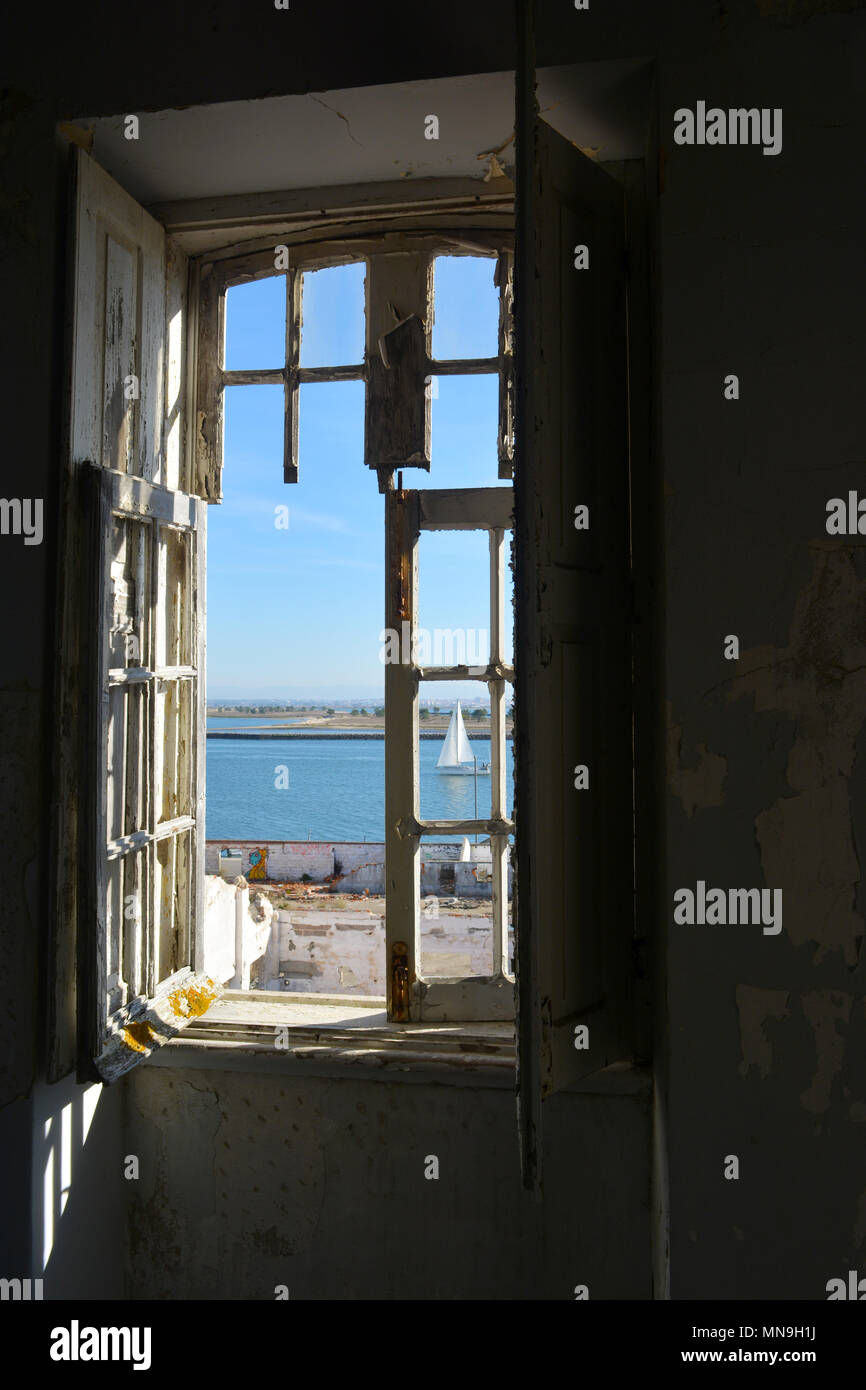 Blick auf einem Segelboot von einem alten, baufälligen Fenster in einer verlassenen Wohnung in Portugal Stockfoto