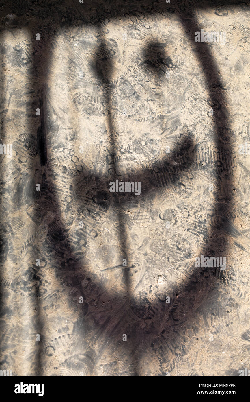 Schatten oder Silhouette der gemalten Smiley auf dem staubigen Spuren eines einsamen ruiniert High Desert Kabinenboden, Mojave, Wonder Valley, Kalifornien, USA. Stockfoto