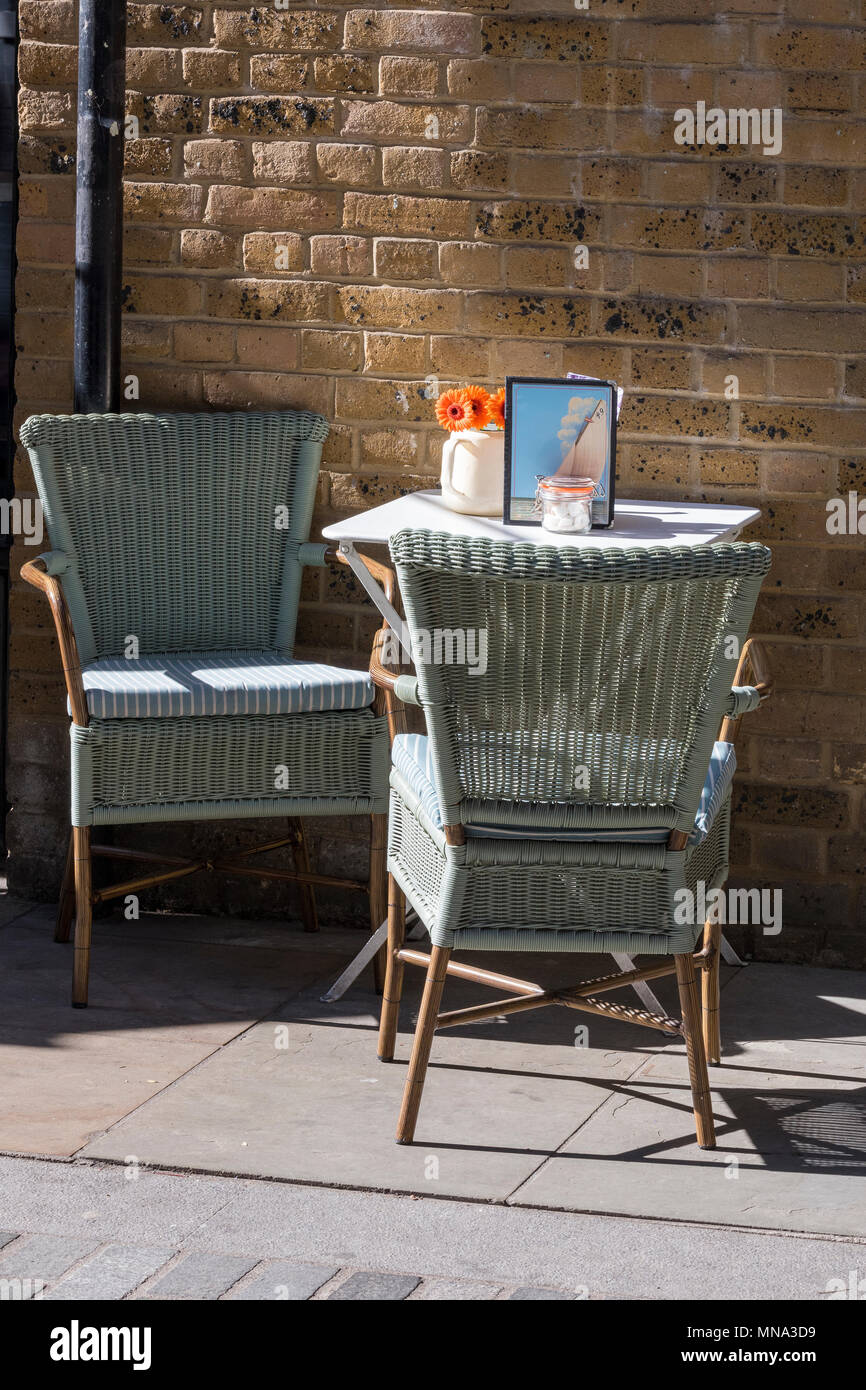 Zwei Korbweide oder korbwaren Stühle an einem kleinen runden Tisch draußen auf der Straße ein kleines Cafe oder Kaffee Haus in einer Gasse von der geschlagenen Schiene London. Stockfoto