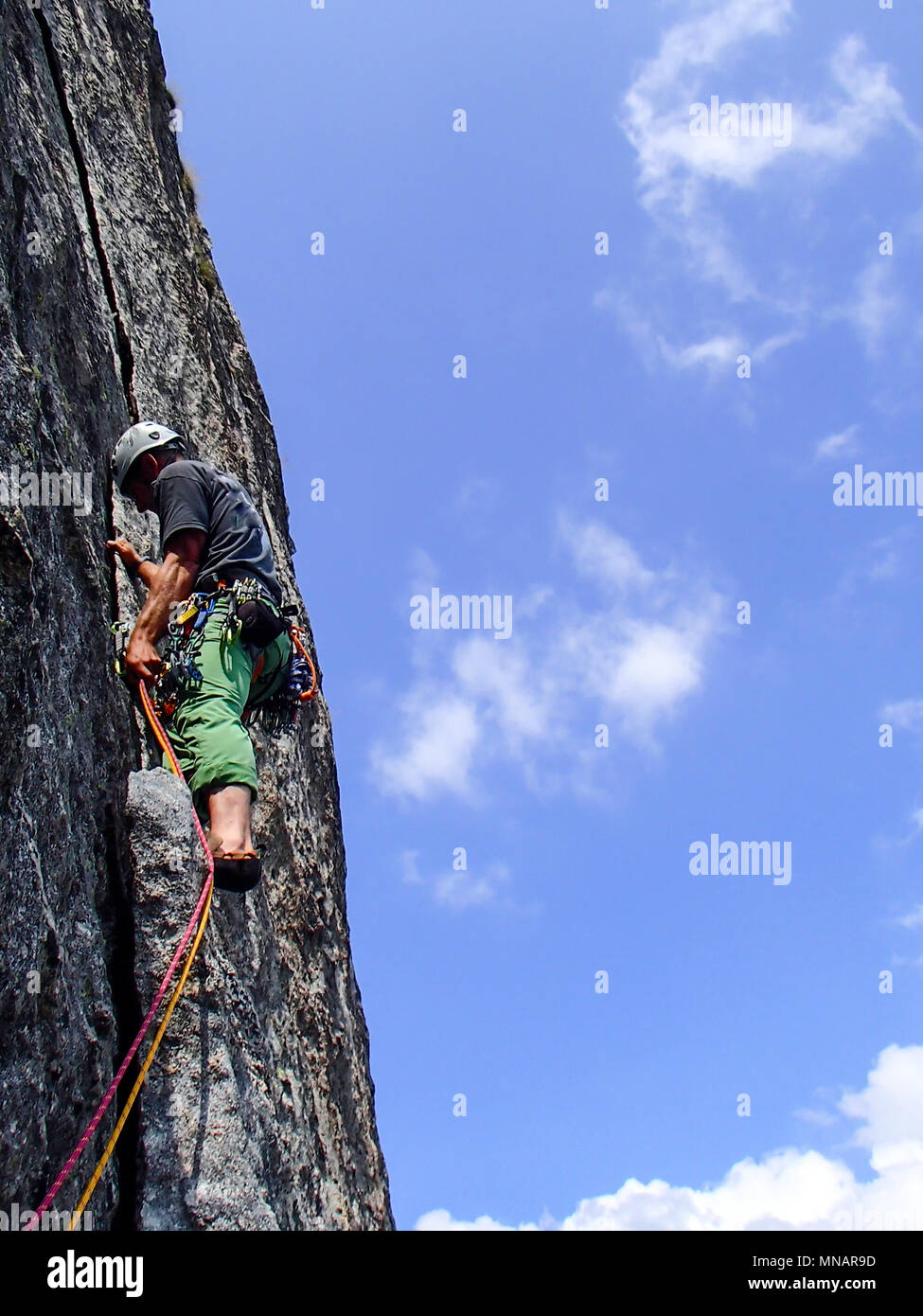 Kletterer in hellen Farben gekleidet auf einem steilen Granit Klettersteig in den Alpen Stockfoto