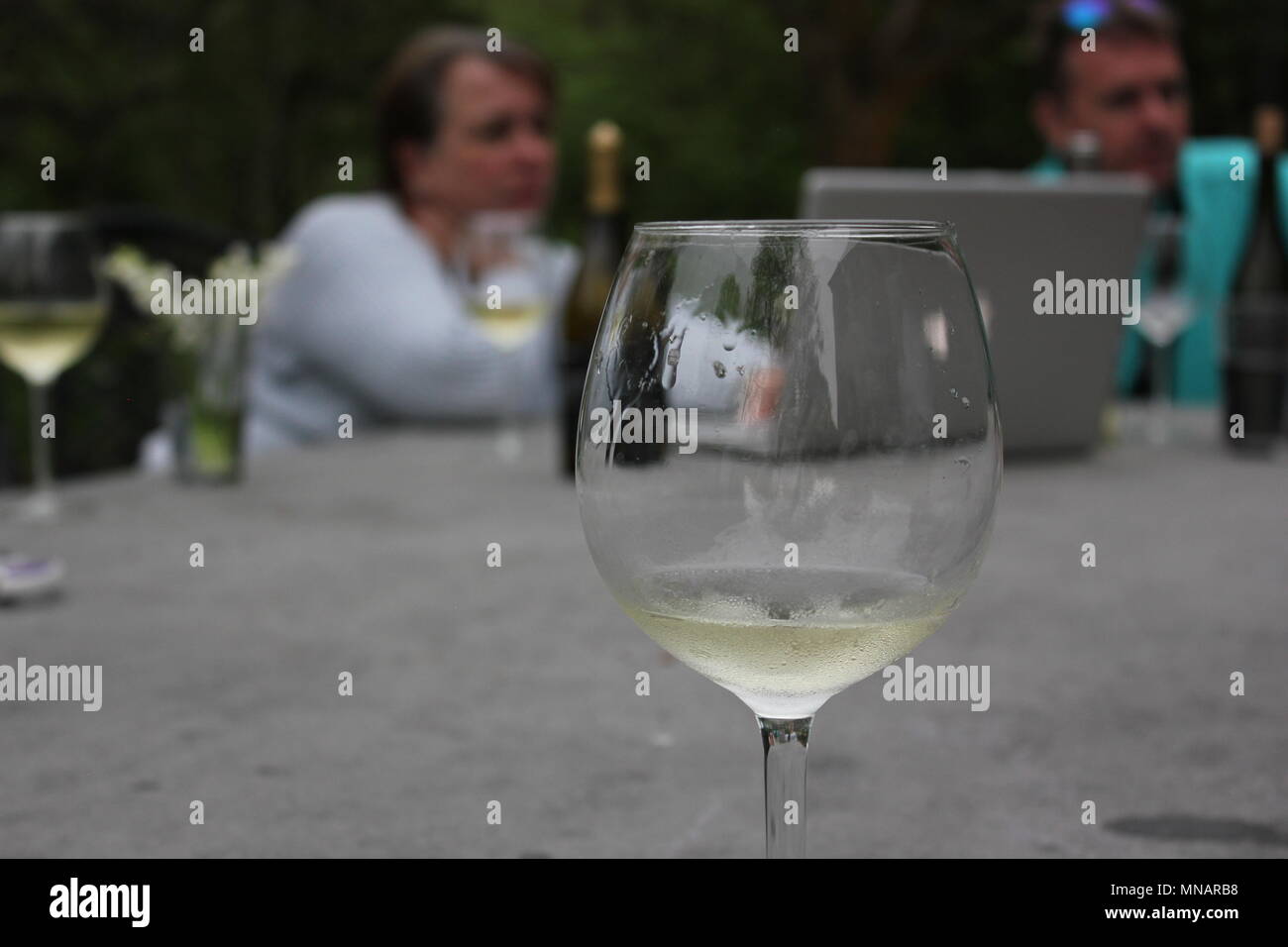 Outdoor Versammlung von Menschen, die vor einem Computer mit einem Glas Wein in den Vordergrund zu lachen. Stockfoto
