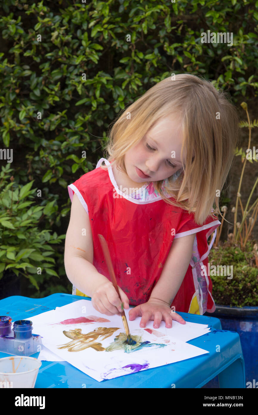 Zwei Jahre altes Mädchen Malerei Bilder und Muster mit Wasserfarben in Garten, malen Sie auf Händen. Schutzkleidung. Stockfoto