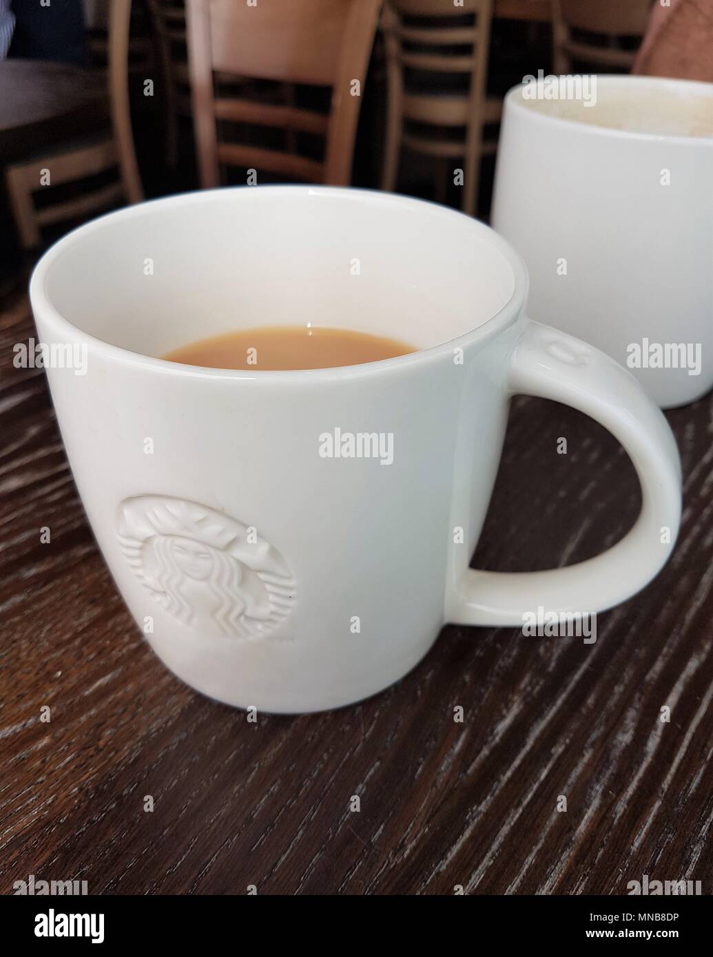 Tasse Kaffee von Starbucks Logo auf einem Tisch mit Stühlen im Hintergrund Stockfoto