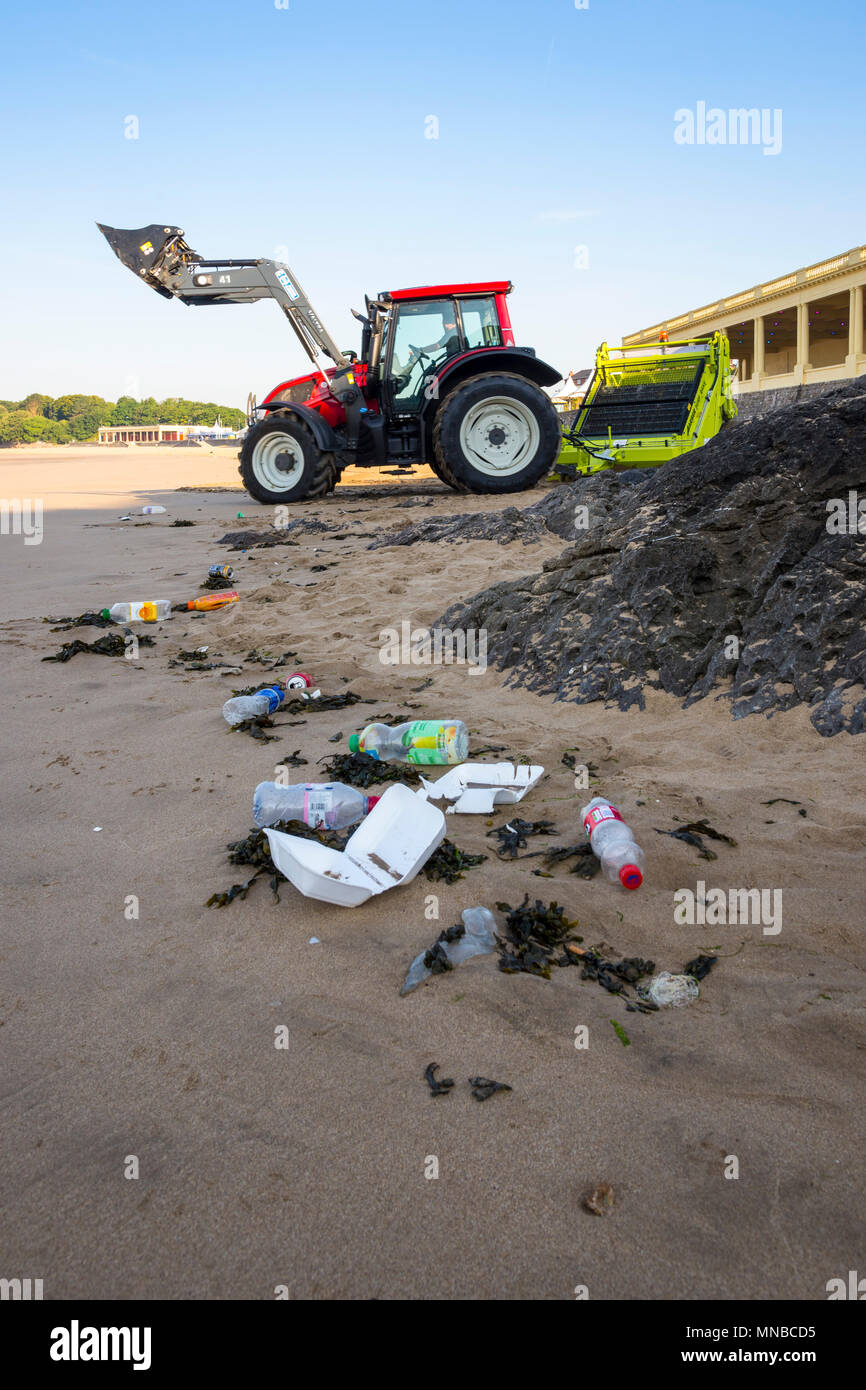 Vordergrund Müll auf ruhigen Sandstrand im Ferienort früh an einem hellen, sonnigen Sommermorgen durch Hintergrund Traktor mit surf Rechen gesäubert werden. Stockfoto