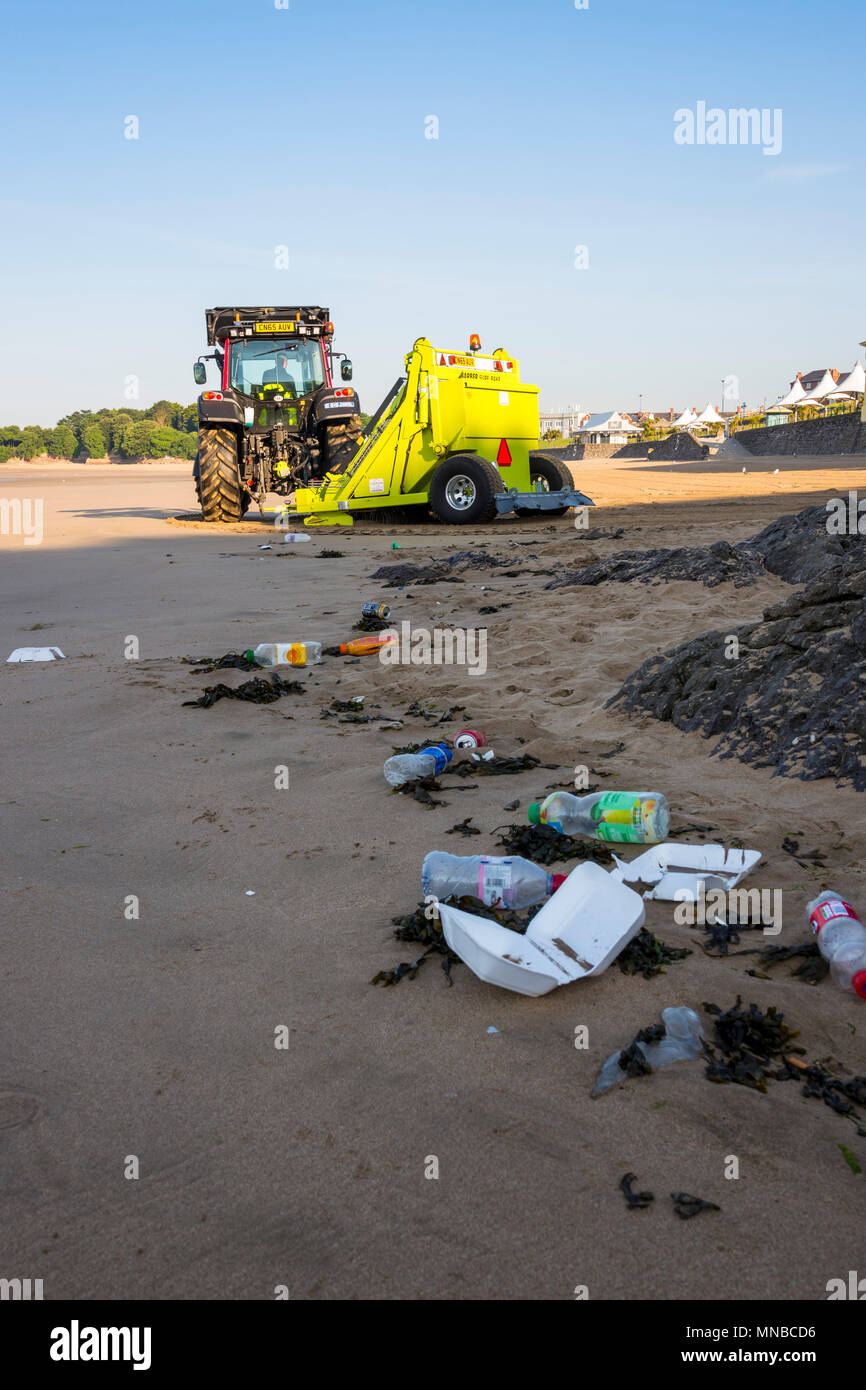 Vordergrund Müll auf ruhigen Sandstrand im Ferienort früh an einem hellen, sonnigen Sommermorgen durch Hintergrund Traktor mit surf Rechen gesäubert werden. Stockfoto