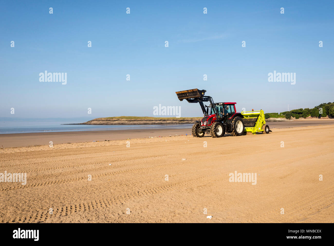 Whitmore Bay Beach bei Barry Island, Wales, früh an einem hellen, sonnigen Sommermorgen der Wurf durch einen roten Traktor ziehen einer Friseur Surfen Rechen gesäubert werden. Stockfoto
