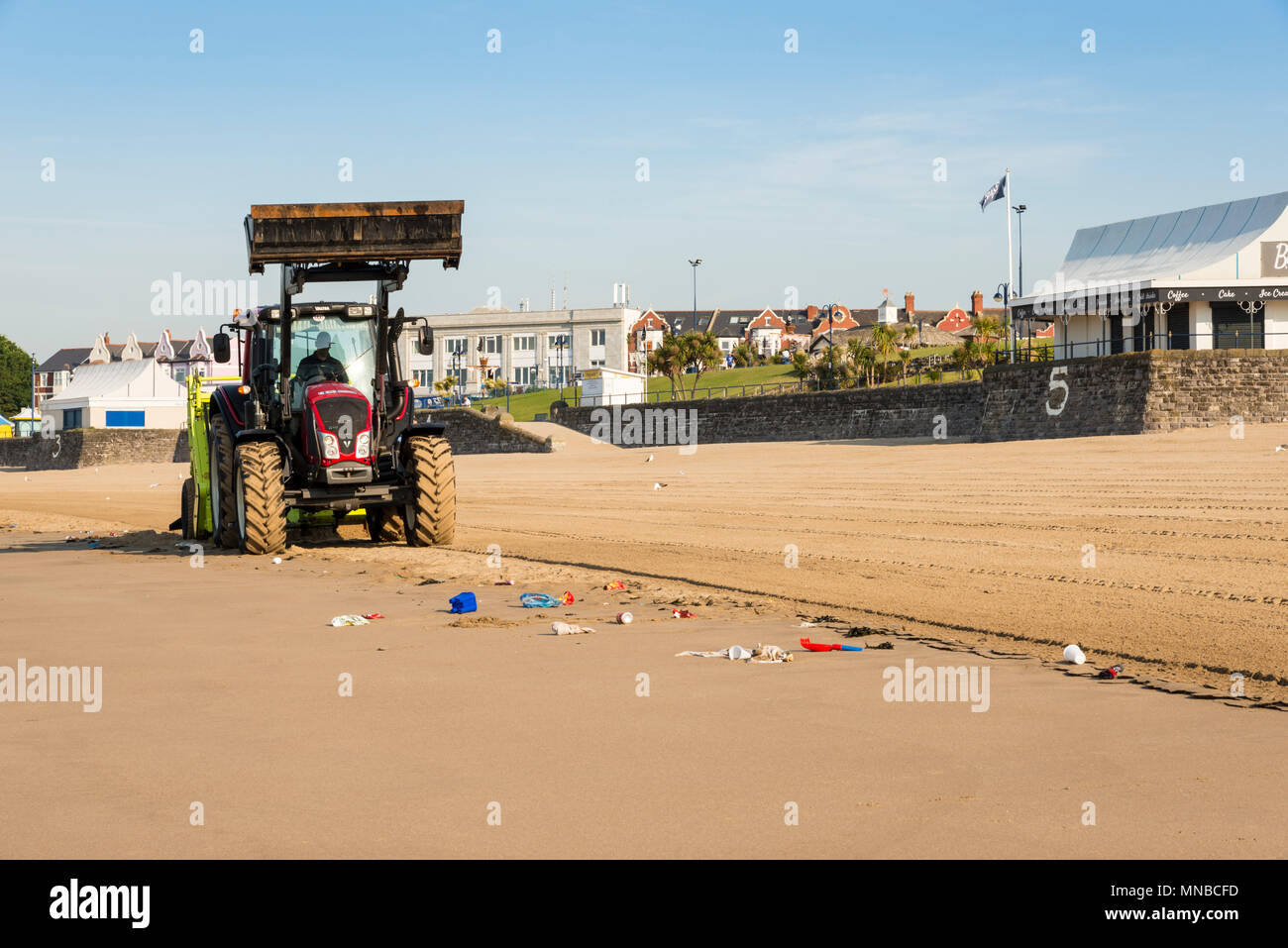 Whitmore Bay Beach bei Barry Island, Wales, früh an einem hellen, sonnigen Sommermorgen der Wurf durch einen roten Traktor ziehen einer Friseur Surfen Rechen gesäubert werden. Stockfoto