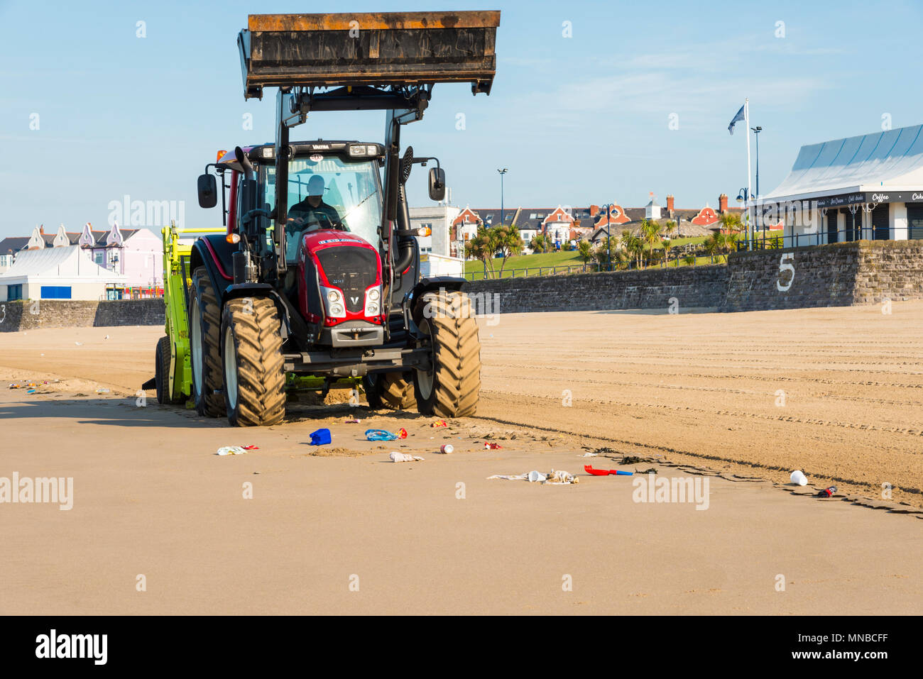 Sandstrand von Barry Island tourist resort mit Wurf auf der tideline von einem großen, roten Traktor mit einem surf Rechen gereinigt werden Stockfoto