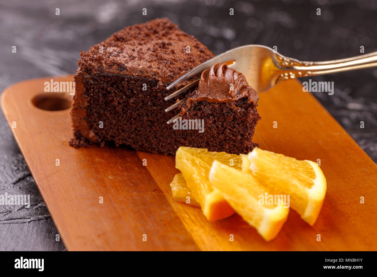 Eine Nahaufnahme Bild von Schneiden in ein Stück Schokolade Kuchen garniert mit Orangenscheiben. Stockfoto