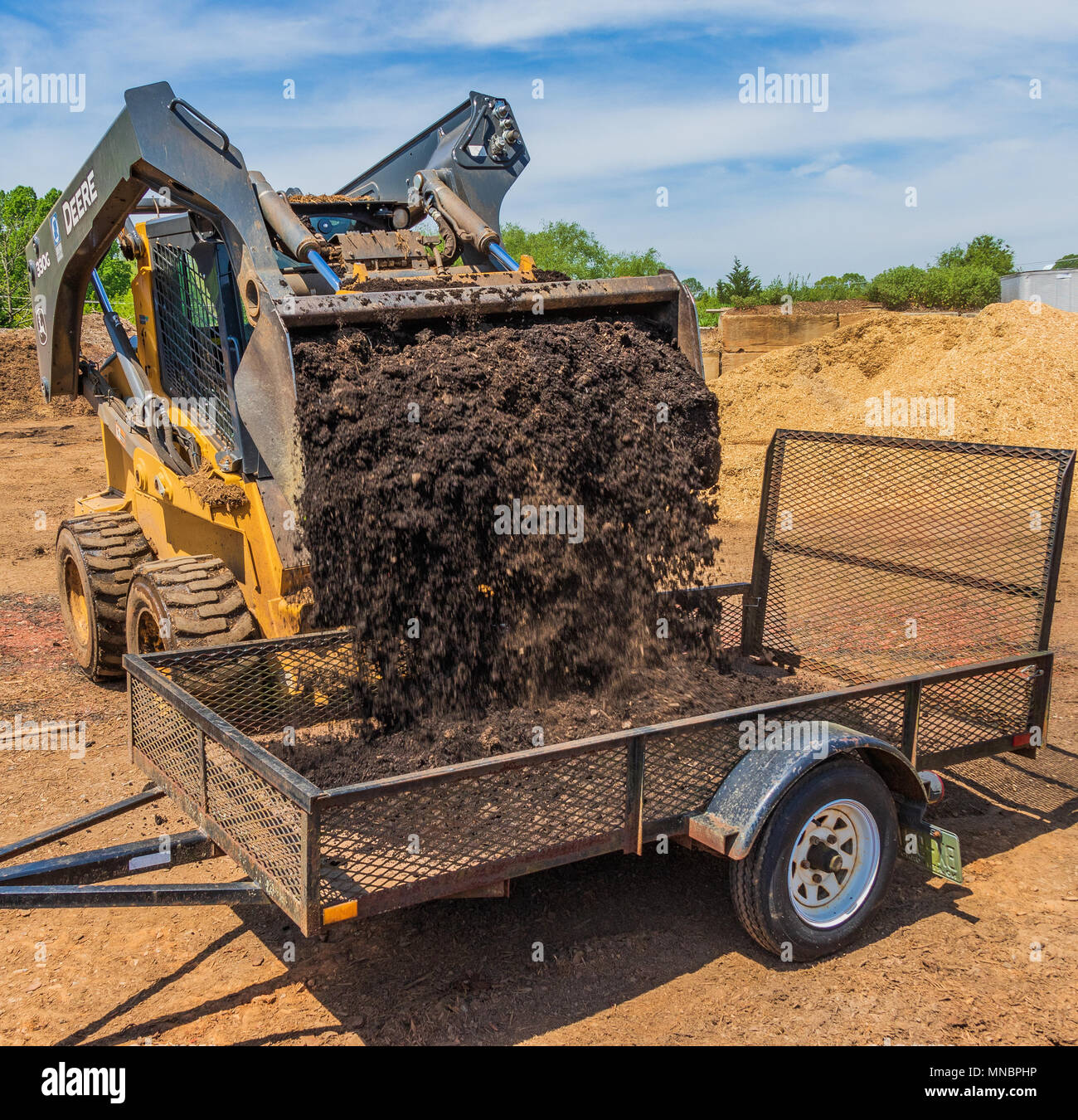 Eine kleine Frontlader ist Dumping reichen Schmutz in einen Anhänger. Stockfoto