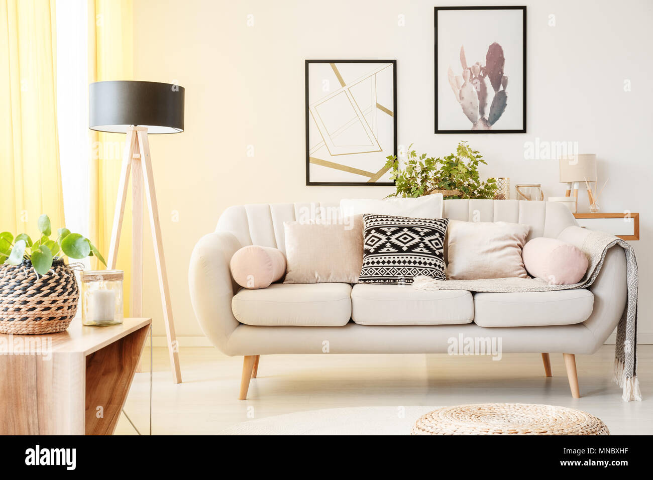 Gemusterten Kissen auf einem beigen Couch neben Lampe und Anlage auf einem  Schrank in einfachen Wohnzimmer mit Poster an der Wand Stockfotografie -  Alamy