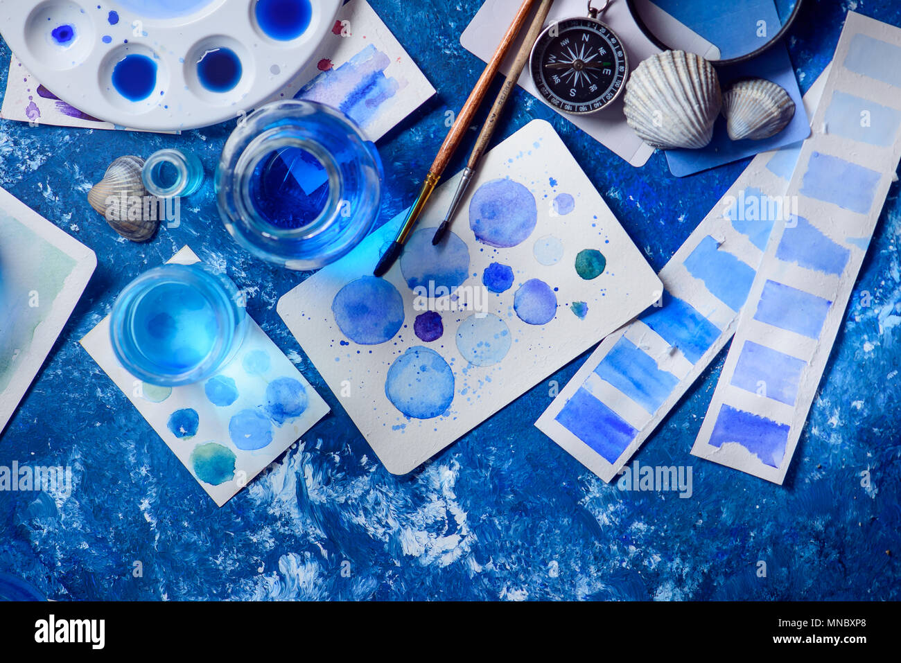 Kreative Künstlerin Arbeitsplatz mit marine Aquarell, Paletten, Muster, Pinsel und Wasser Gläser von oben. Malerei Meer Konzept auf einem marine blau backgroun Stockfoto