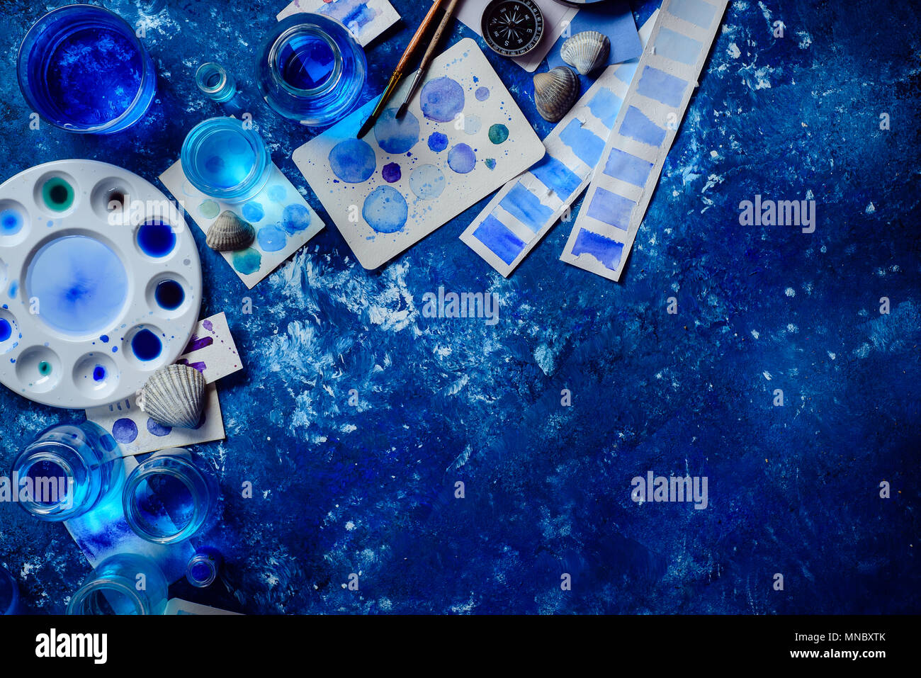 Kreative Künstlerin Arbeitsplatz mit marine Aquarell, Paletten, Muster, Pinsel und Wasser Gläser von oben. Malerei Meer Konzept auf einem marine blau backgroun Stockfoto