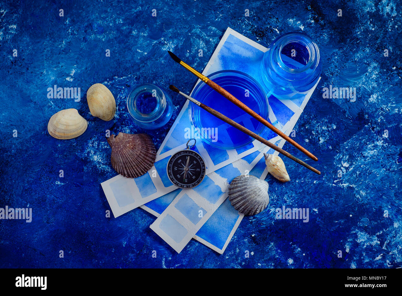 Kreative Künstlerin Arbeitsplatz mit marine Aquarell, Paletten, Muster, Pinsel und Wasser Gläser von oben. Malerei Meer Konzept auf einem marine blau backgroun Stockfoto