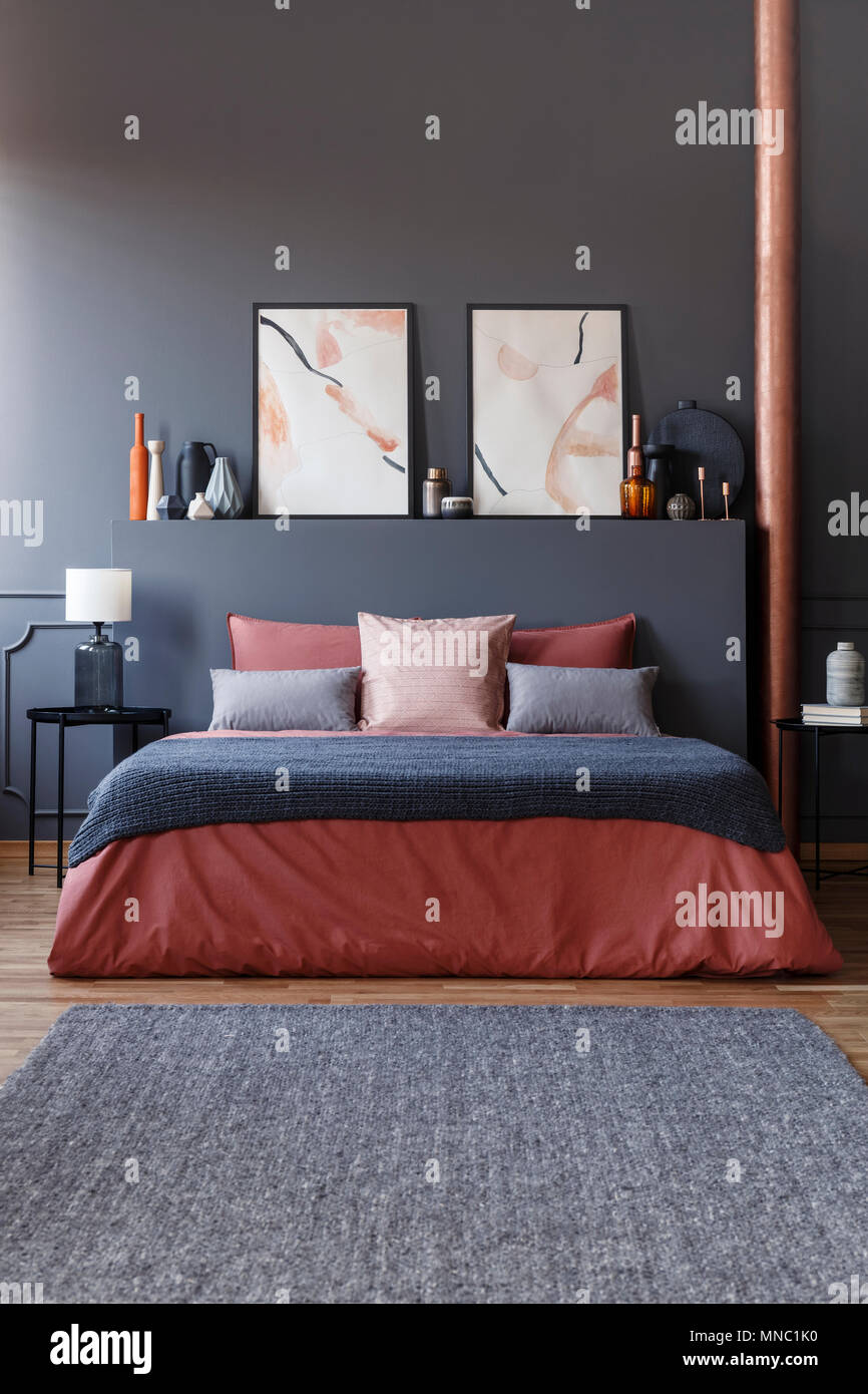 Vorderansicht eines gemütlichen Bett mit Ingwer Bettwäsche, graue Decke und Kissen in dunklen Schlafzimmer Innenraum mit schwarzen Nachttischen, Aquarell Plakate und Eleg Stockfoto