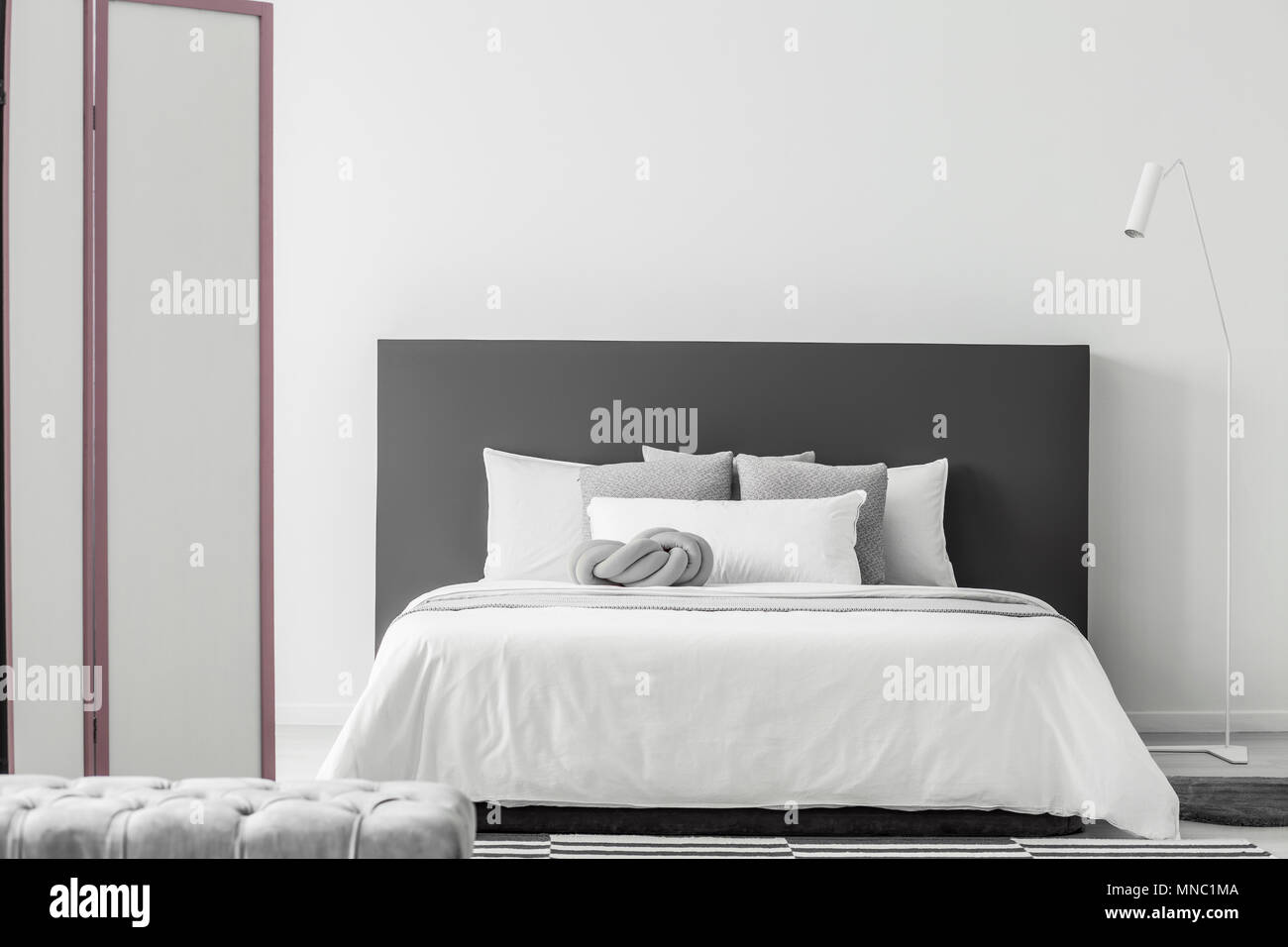 Weiße Lampe neben dem Bett mit grauen bedhead in minimalen Schlafzimmer  Innenraum mit Pouf und Bildschirm Stockfotografie - Alamy