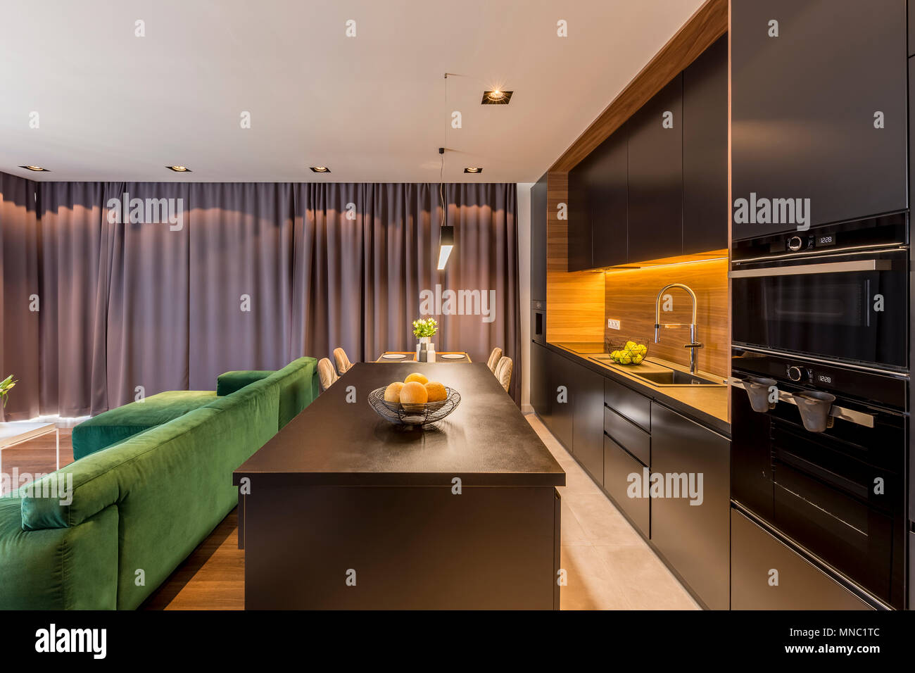 Küche Insel in dunklen open space Interieur mit grünen Couch und braunen Vorhängen Stockfotografie