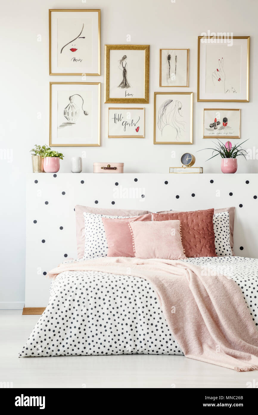 Rosa pastell Decke auf gemusterte Bettwäsche in femininen Schlafzimmer Innenraum mit Galerie der Poster Stockfoto