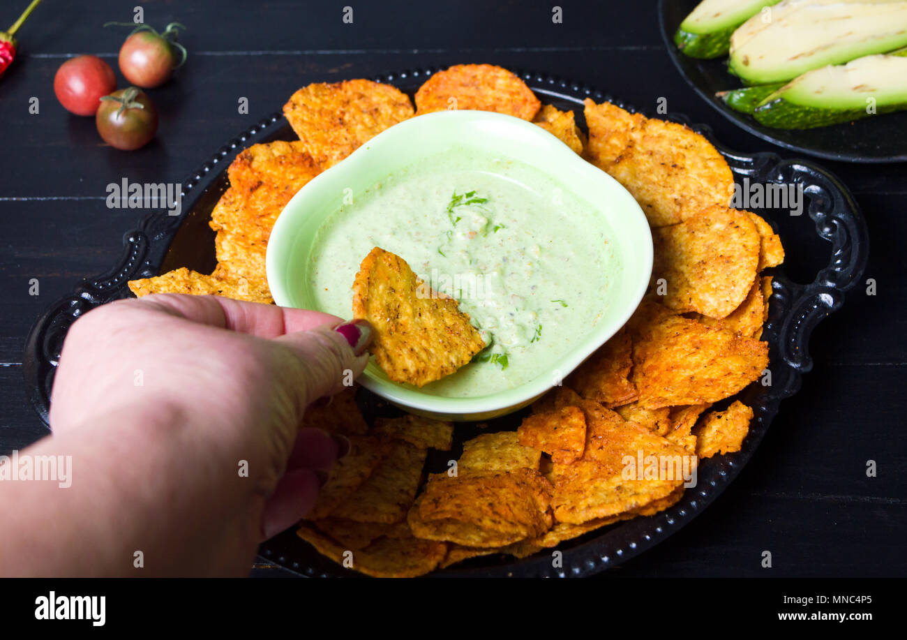 Hand tauchen Tortilla Chips in Grün dip auf einer Platte Stockfoto