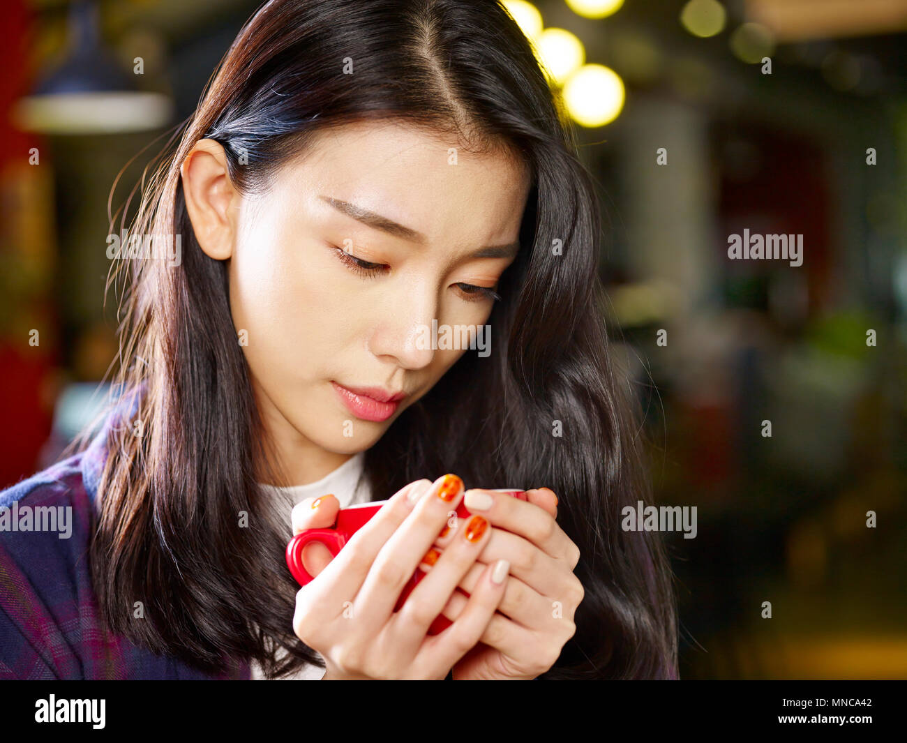 Schöne junge Asiatin bei einer Tasse Kaffee mit ernsten Gesichtsausdruck. Stockfoto