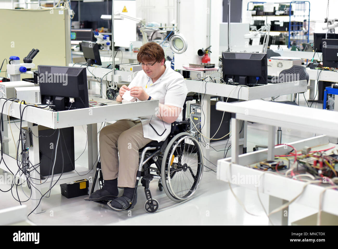 Behinderte Arbeitnehmer in einem Rollstuhl Montage elektronischer Bauteile in ein modernes Werk am Arbeitsplatz Stockfoto