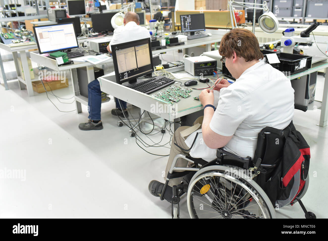 Behinderte Arbeitnehmer in einem Rollstuhl Montage elektronischer Bauteile in ein modernes Werk am Arbeitsplatz Stockfoto