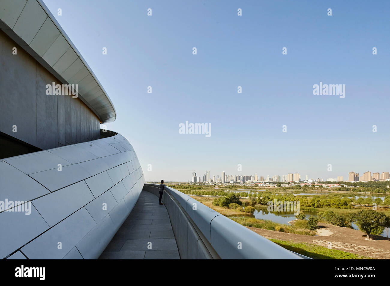 Erhöhte Ansicht von der Rampe, über Feuchtgebiete auf die Skyline der Stadt. Harbin Opernhaus, Harbin, China. Architekt: MAD, 2015. Stockfoto