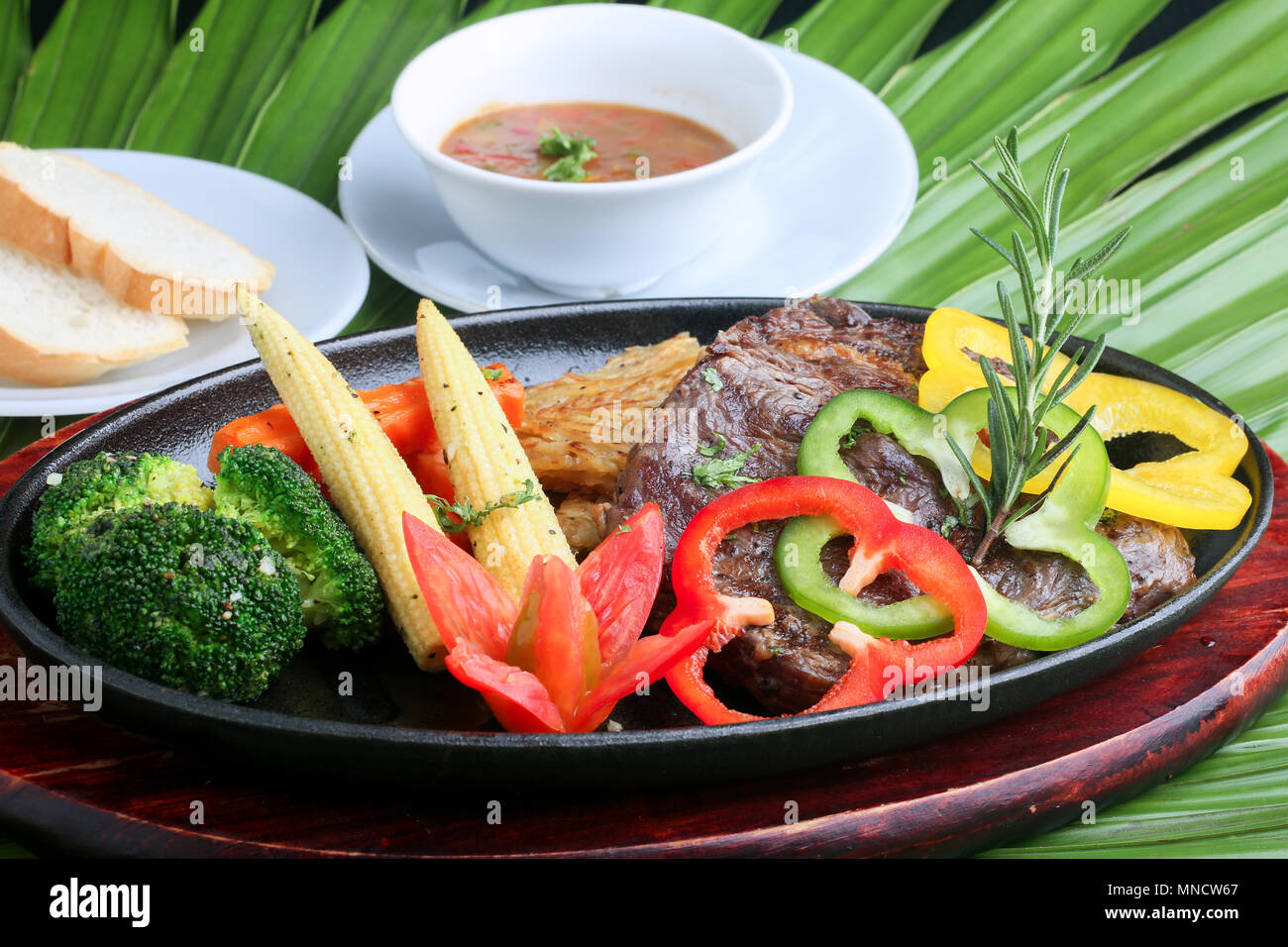 Rindersteak - BBQ Strip Steak (gegrilltes Rindfleisch Strip Lenden Steak) mit gebratenem Gemüse und weißer Soße, Salat Dressing und Brötchen. Stockfoto