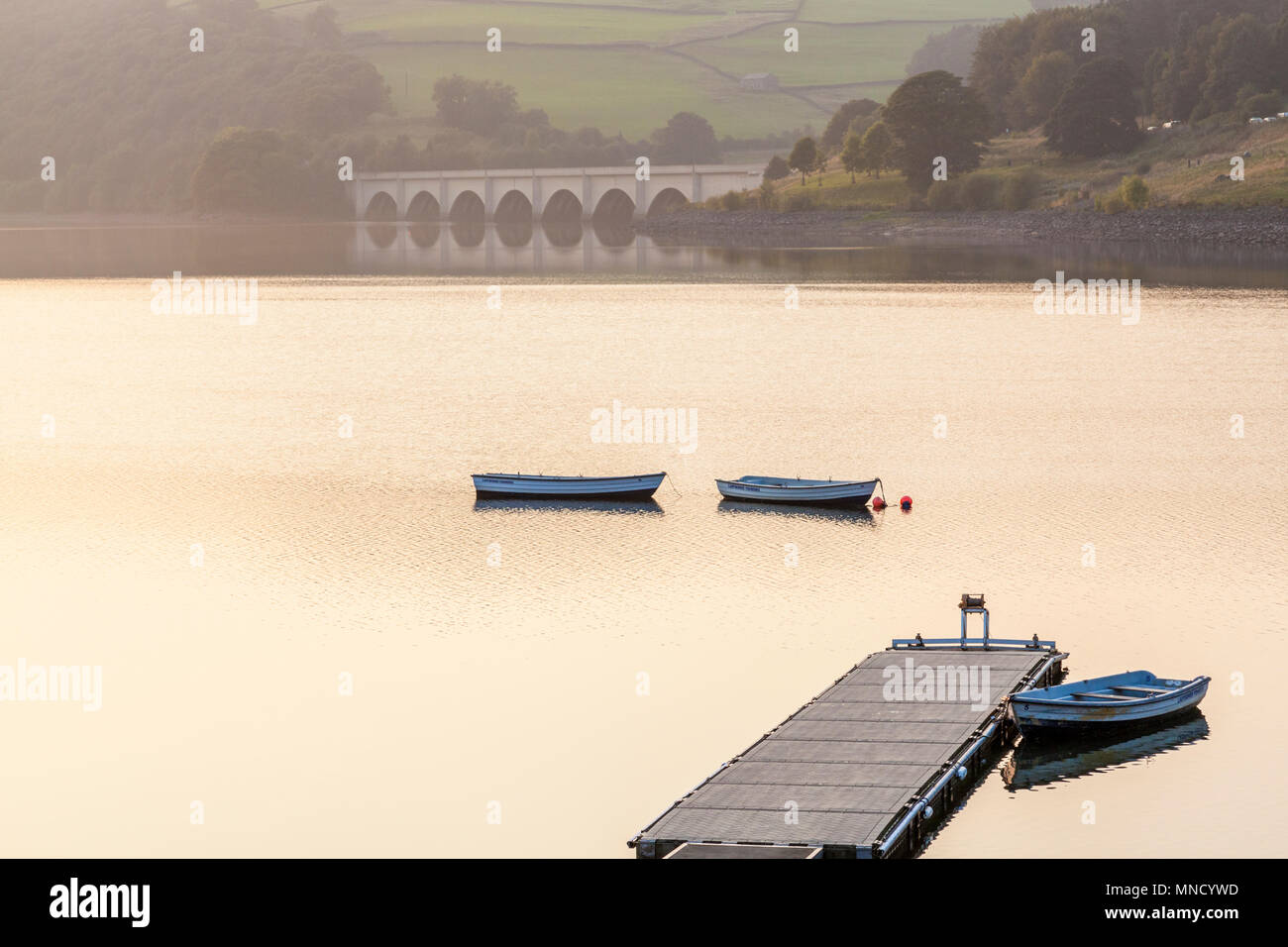 Jetty und drei Ruderboote in der Dämmerung auf dem Wasser bei Ladybower Reservoir. Ashopton Viadukt ist in der Ferne. Peak District, Derbyshire, England, Großbritannien Stockfoto