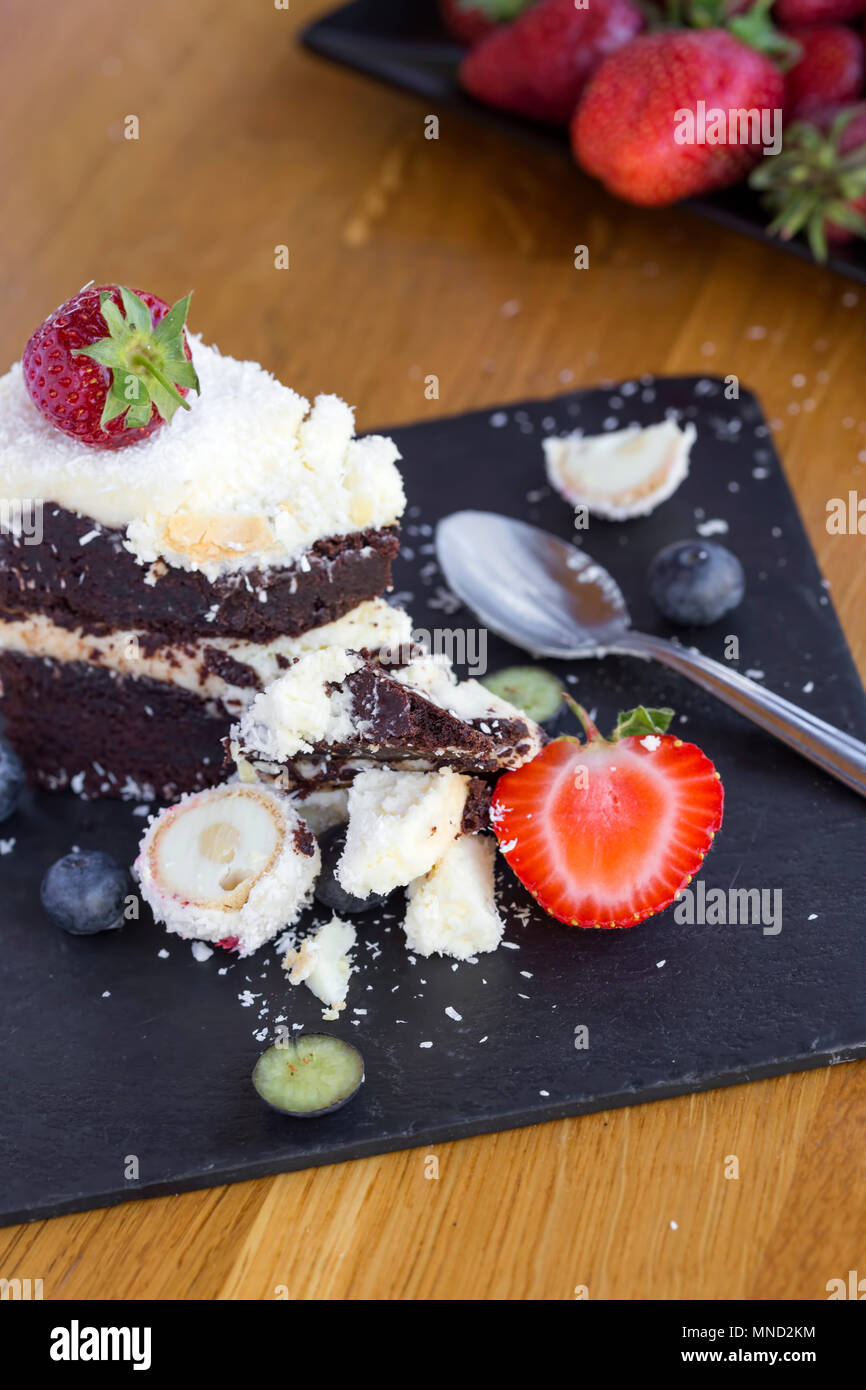 Essen leckere Schokolade Kuchen mit weißer und dunkler Schokolade, Früchte und Kokosnuss auf Schiefer Stockfoto
