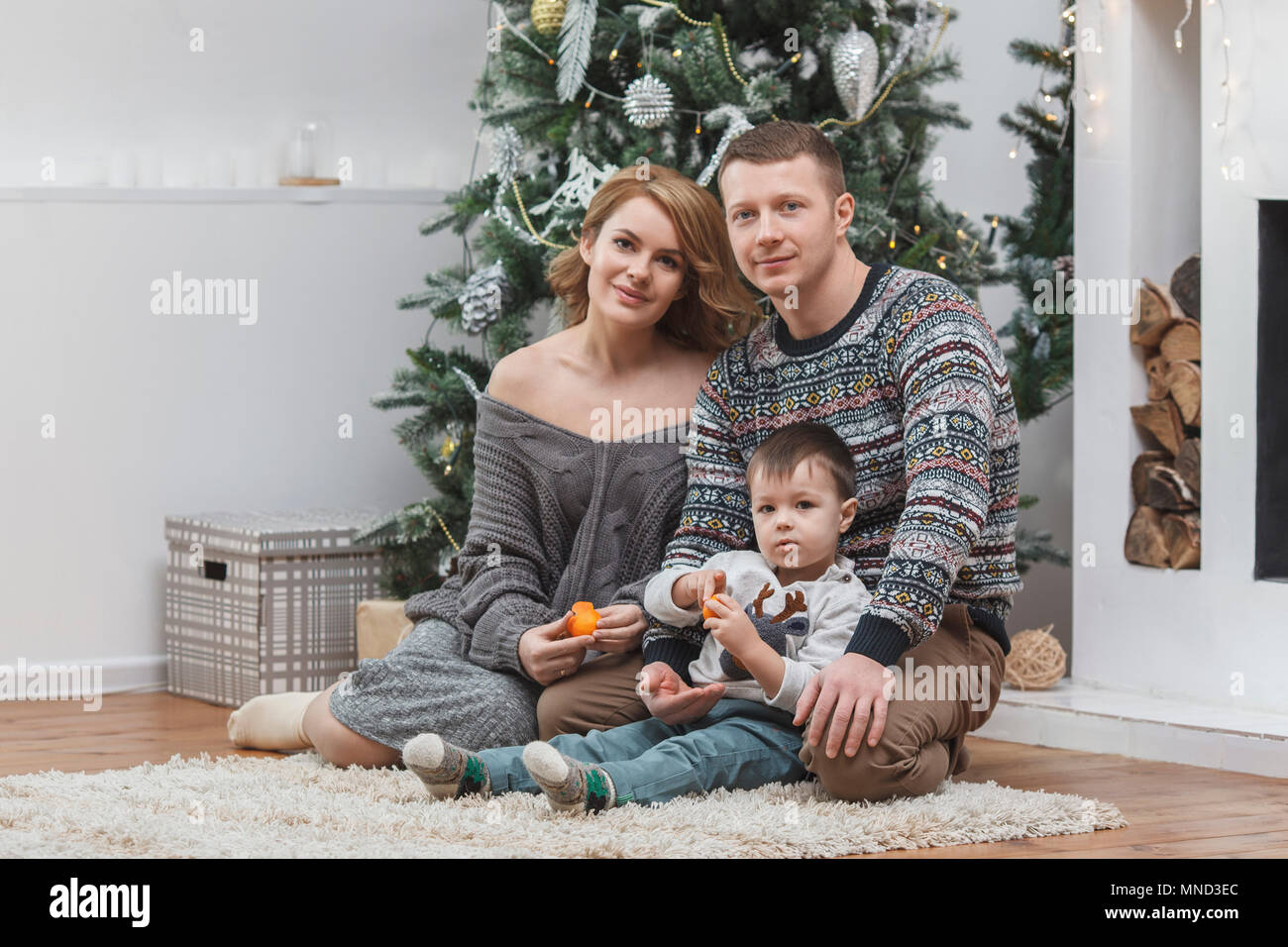 Portrait von Vater und Mutter mit Sohn auf Teppich gegen Weihnachtsbaum zu Hause Stockfoto