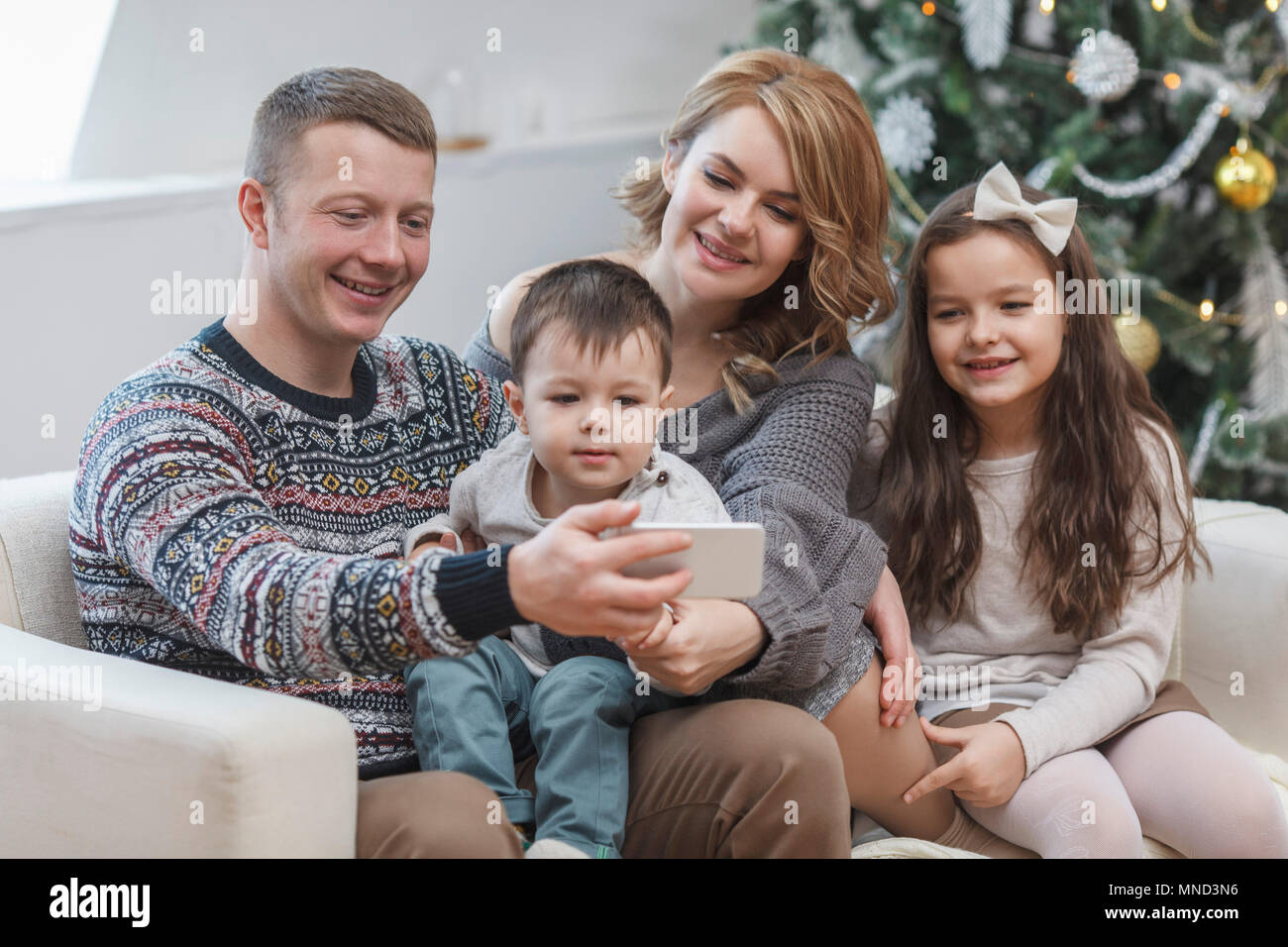 Glückliche Menschen teilen Handy mit Familie auf dem Sofa zu Hause während Weihnachten Stockfoto