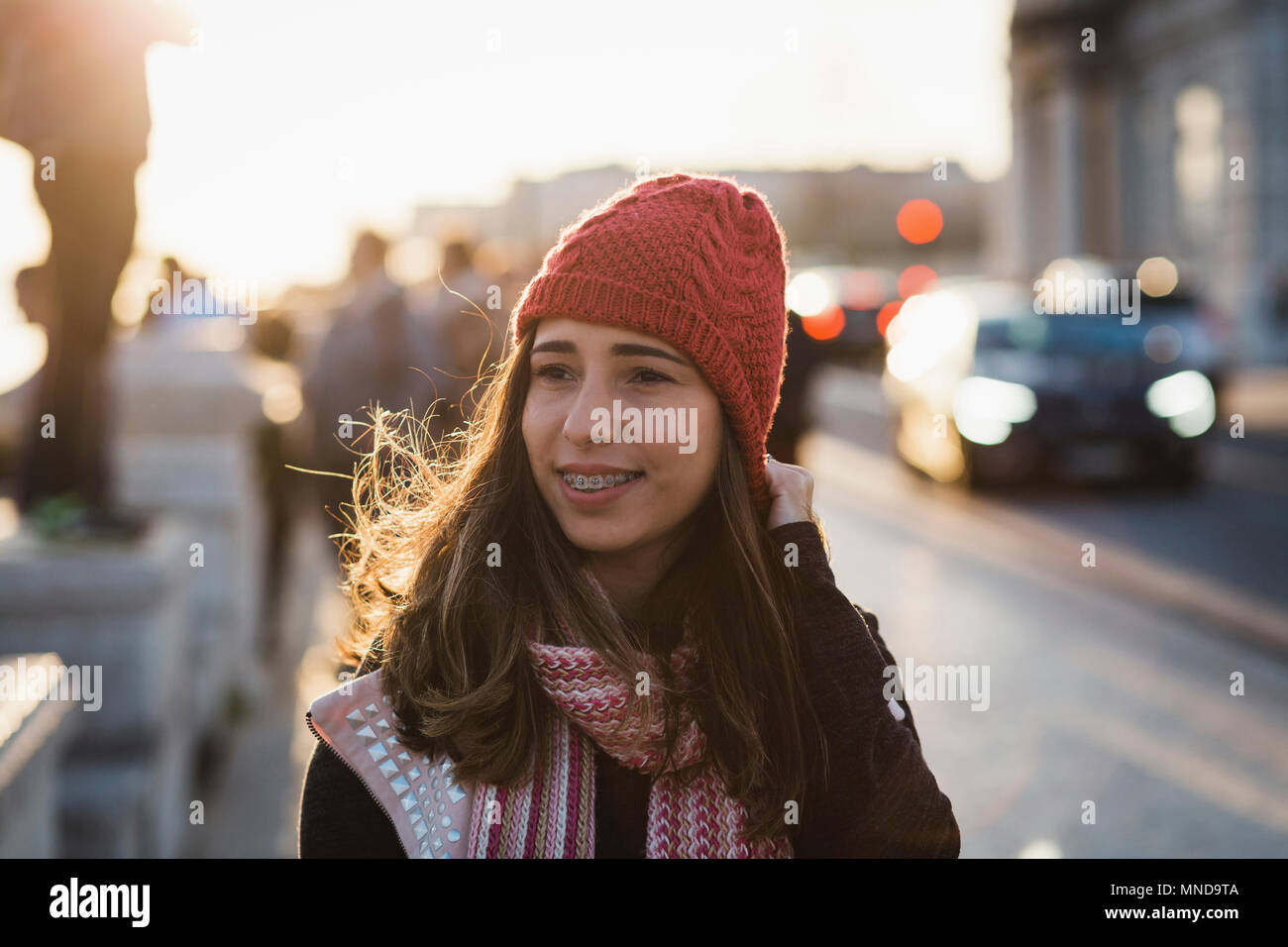 Lächelnd Mitte der erwachsenen Frau tragen Stricken hat zu Fuß in die Stadt bei Sonnenuntergang Stockfoto
