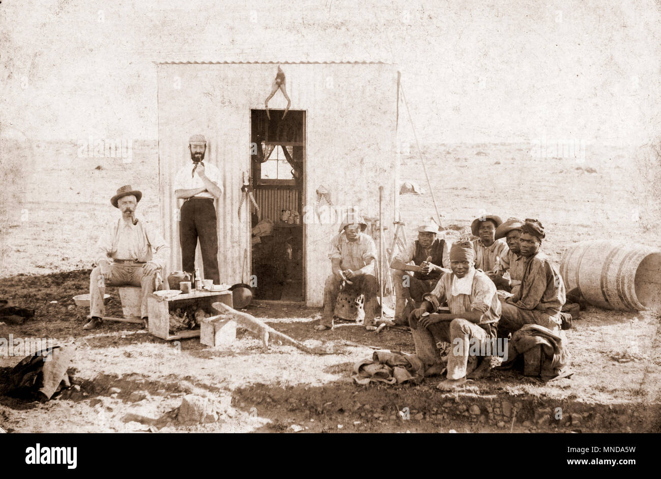 Zwei weiße Männer mit Hut und Gruppe von sechs schwarze Männer, vermutlich ein Steinbruch oder Mine in Südafrika. Hinweis: Die Werkzeuge aufhängen und die große Eidechse im Vordergrund, vermutlich 1890s Stockfoto